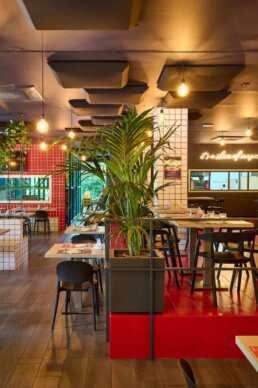 Vista d’insieme della Pizzeria Luna Rossa con soffitto fonoassorbente e dettagli vegetali, progetto acustico di 2B Resine.