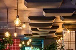 Dettaglio dei pannelli fonoassorbenti sospesi e delle lampade a sospensione nella Pizzeria Luna Rossa, installazione acustica curata da 2B Resine.